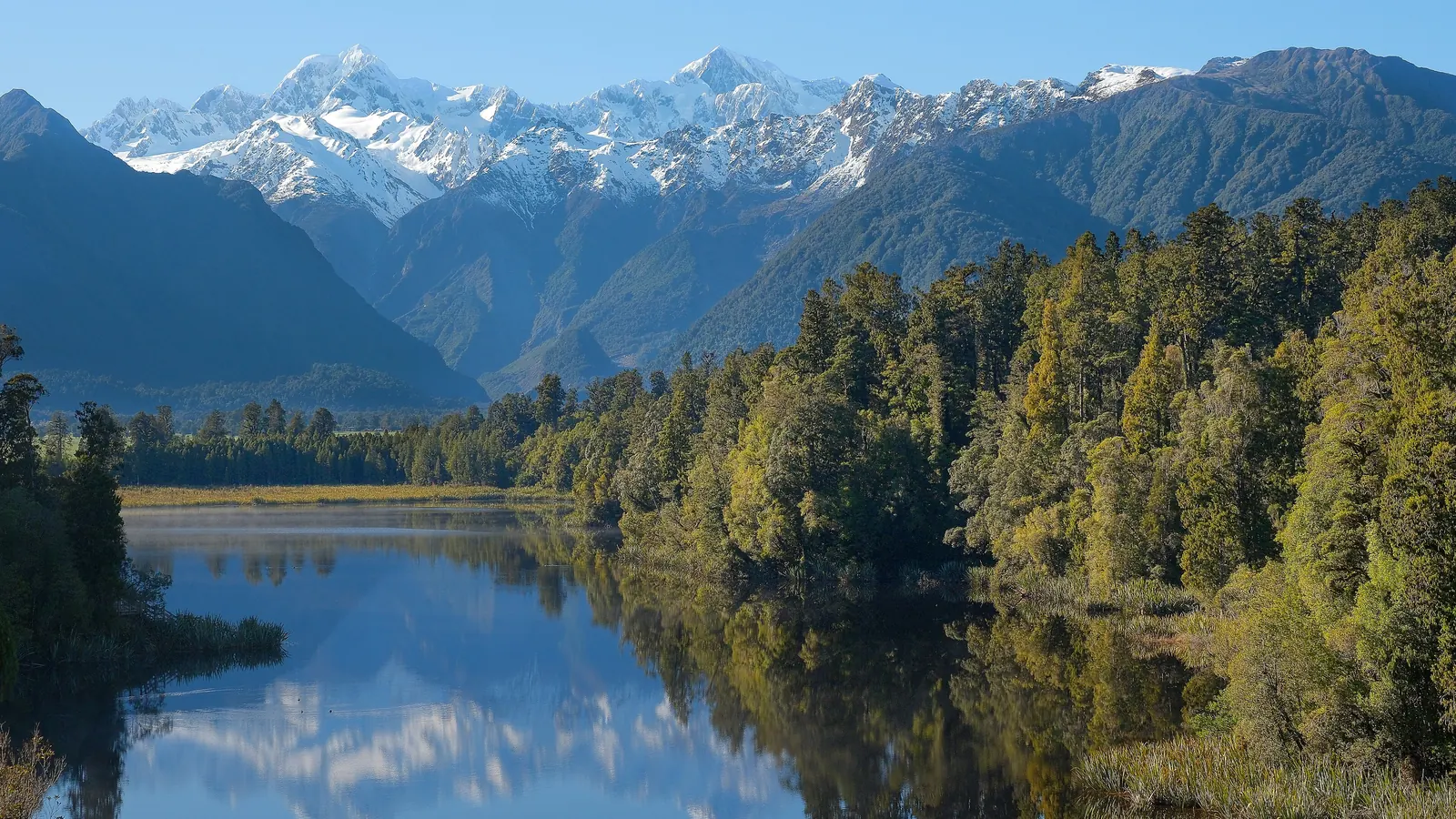 Snow-covered Aoraki / Mount Cook and Mount Tasman reflected in the dark, still water of Lake Matheson