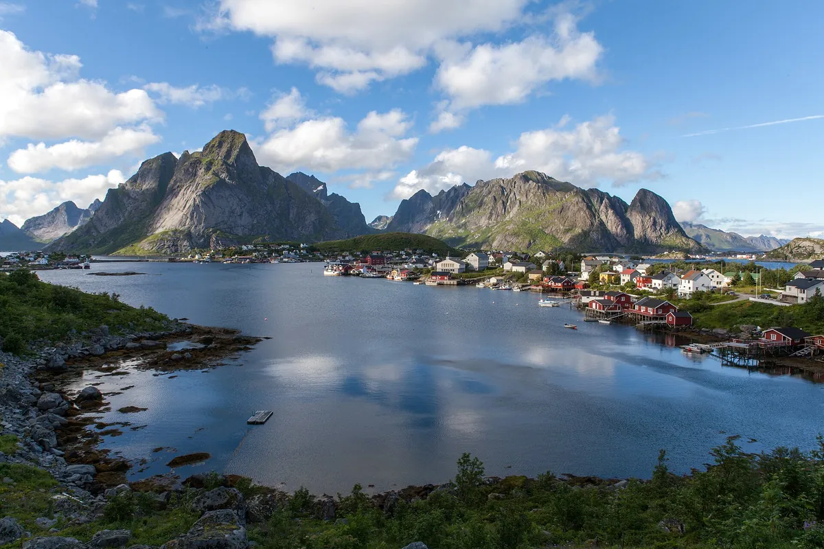 The fishing village of Reine beside a calm fjord, ringed by steep green peaks