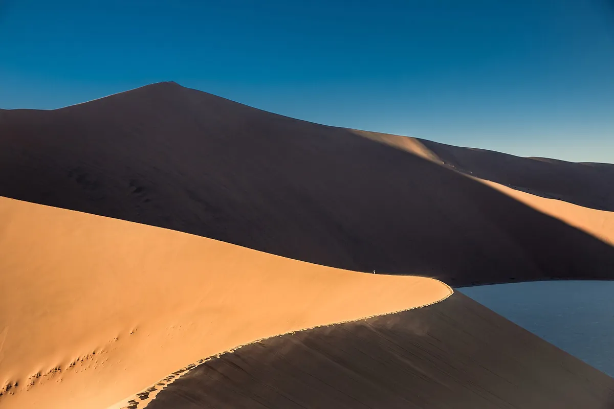 A towering orange sand dune at Sossusvlei, one face lit by the sun and the other in deep shadow